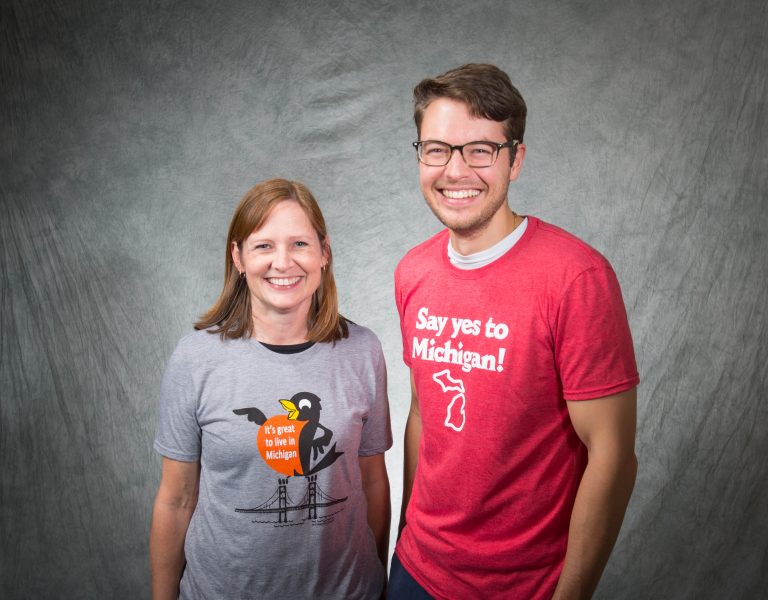 A man and woman posing for a photo - each wearing a t-shirt with a Michigan Tourism slogan on it.